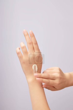 Foto de Manos de modelo de mujer aplicando textura crema cosmética en su mano sobre un fondo claro. Concepto de rutina diaria de cuidado de la piel y del cuerpo - Imagen libre de derechos