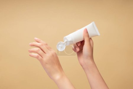 Photo for Hand model holding an empty label tube in white color over a beige background. Cosmetic branding product mockup - Royalty Free Image