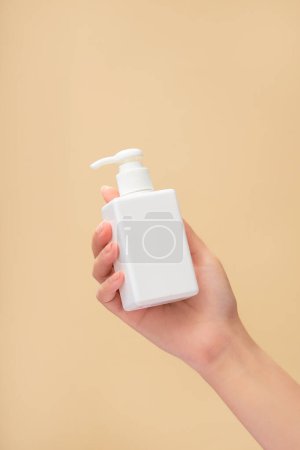 Téléchargez les photos : Un modèle féminin tenant une étiquette vide pompe distributeur de bouteilles en blanc. Promotion de produits nettoyants ou shampooings - en image libre de droit
