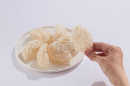 A dish with edible bird nest placed on and a hand model holding an edible bird nest on white background. Traditional medicine to enhance health and skin condition