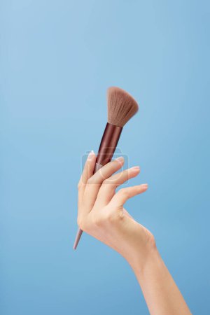 Photo for A beautiful hand model is carrying an angled brush over a light blue background. Cosmetic product promotion - Royalty Free Image