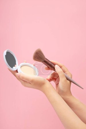Photo for Against a pink pastel background, female hand model is carrying a compact powder and an angled brush. A set of various products for makeup - Royalty Free Image