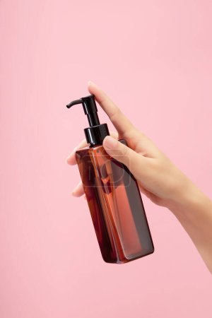 Photo for Woman hand model holding a pump bottle dispenser over a light pink background. Beauty and cosmetic for healthy skin concept. Mockup - Royalty Free Image
