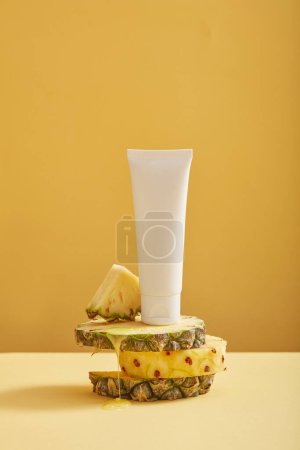 Téléchargez les photos : Les tranches d'ananas de forme ronde sont empilées et un tube blanc avec une étiquette vide placée sur le dessus. Modèle de produit avec extrait d'ananas (Ananas comosus) - en image libre de droit
