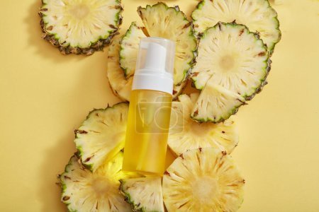 Photo for A transparent bottle filled with yellow liquid displayed on a pile of pineapple slices. Product mockup of pineapple (Ananas comosus) extract - Royalty Free Image