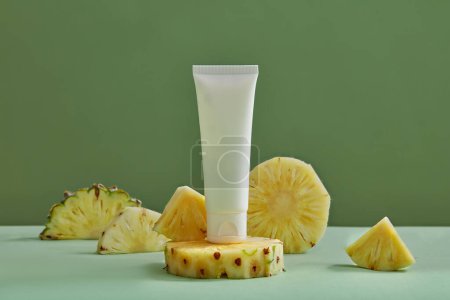 Photo for A white tube without label standing on pineapple slice decorated on green background. Using skin care product extracted from pineapple (Ananas comosus) for brighter skin - Royalty Free Image
