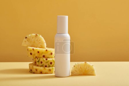 Foto de Una botella de etiqueta vacía en color blanco decorada con rodajas de piña (Ananas comosus) sobre fondo claro. La piña tiene muchos beneficios para la piel y el cabello - Imagen libre de derechos