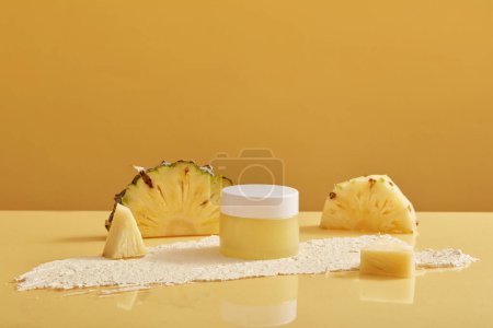 Téléchargez les photos : Un pot de gommage extrait de l'ananas (Ananas comosus) décoré de tranches d'ananas et réfléchi sous celui-ci. Ingrédient pour la fabrication de cosmétiques - en image libre de droit