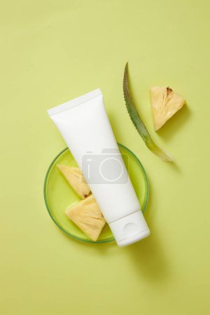 Photo for Top view of an empty label white tube placed on a glass petri dish containing essence extracted from pineapple and pineapple slices. Cosmetic product mockup - Royalty Free Image