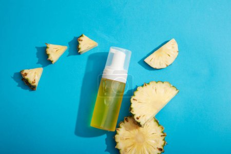 Photo for An empty label bottle filled with yellow liquid extracted from pineapple (Ananas comosus) decorated on blue background. Pineapple contains a lot of vitamin C to help improve healthy and bright skin - Royalty Free Image