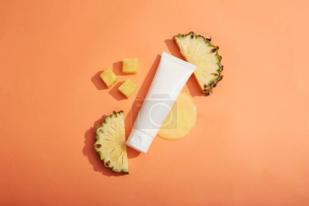 Ein leerer Etikettenschlauch, der auf minimalem Hintergrund mit Essenzflüssigkeit und Ananasscheiben und -würfeln verziert ist. Ananas (Ananas comosus) ist reich an AHA, das abgestorbene Hautzellen abschält