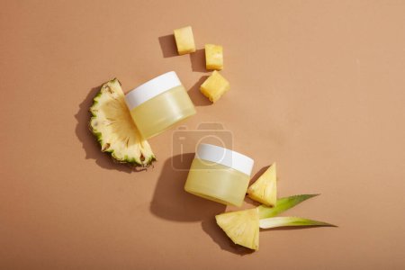Photo for Flat lay of empty label jars arranged on brown background with pineapple slices. Cosmetic product mockup extracted from pineapple (Ananas comosus), it can enhance skin and hair condition - Royalty Free Image