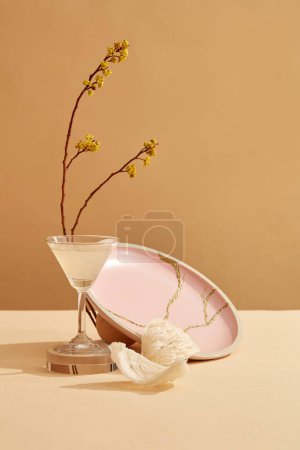 A glass containing bird nest soup placed on podium, next to it is edible bird nest, a pattern plate and flower branch. Bird nest helps boosting collagen production and moisturizing the skin