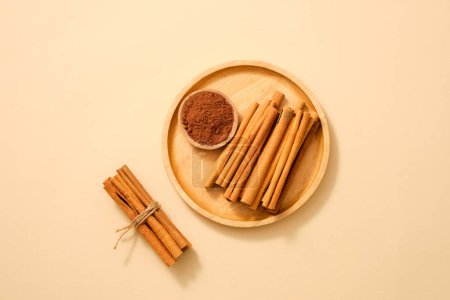 Foto de Un plato de madera con varillas de canela y canela en polvo colocado en. Canela (Cinnamomum) es utilizable para cocinar, curación e ingrediente para cosméticos - Imagen libre de derechos