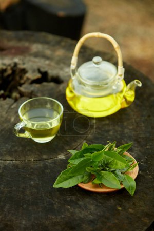 On a wooden pedestal, there is a tea set with a teapot, a tea cup, and a dish of green tea leaves. Healthy concept. Good for your health, mind and body