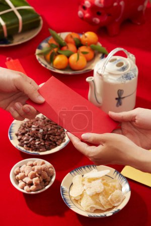 Foto de Una mesa decorada en rojo para la celebración del Año Nuevo Lunar con comida y bebida. Gente dándose suerte el uno al otro - Imagen libre de derechos