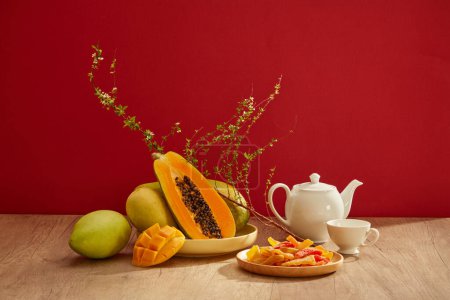 Foto de Muchos tipos de frutas con algunos dulces secos en un plato y un juego de té colocado en la mesa de madera con fondo rojo. Vista frontal - Imagen libre de derechos