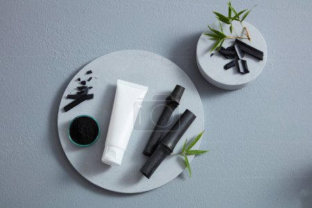 Photo for White cosmetic tube between an activated charcoal bowl and black bamboo, placed on big circle podium. Top view - Royalty Free Image