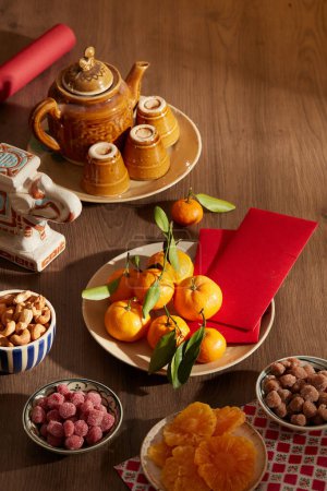 Foto de Tetera con tazas, anacardos, mandarinas, sobres rojos y algunas frutas confitadas secas sobre mesa de madera - Imagen libre de derechos