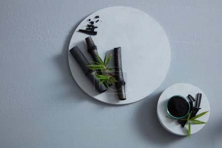 Foto de Bambú negro y un tazón de carbón negro en polvo colocado en podios blancos con vista superior. Espacio en blanco para publicidad, contenido abstracto - Imagen libre de derechos