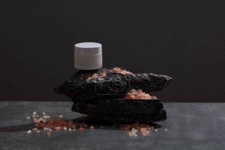 Téléchargez les photos : Un pot de gommages sur une pierre noire avec du sel rose himalayen éparpillé autour - en image libre de droit