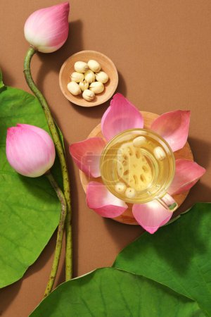 Flor de loto (Nelumbo nucifera), brote de loto, semillas de loto decoradas sobre un fondo marrón minimalista con hojas verdes. Vista desde arriba