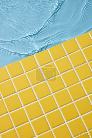 Téléchargez les photos : Carreaux de mosaïque jaune fond avec de l'eau bleue pour concept d'été. Espace vide. Vue du dessus - en image libre de droit
