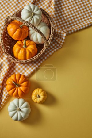 A basket of halloween pumpkins placed on a napkin decorated on yellow background. Flat lay