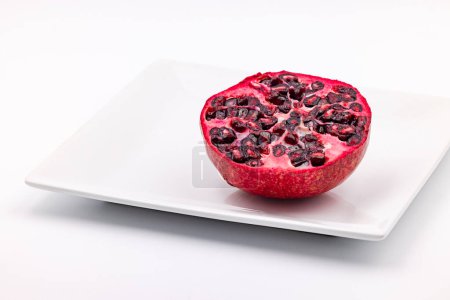 Photo for Studio shot of half a pomegranate striking red exposed on a white plate cut out on a white background - Royalty Free Image