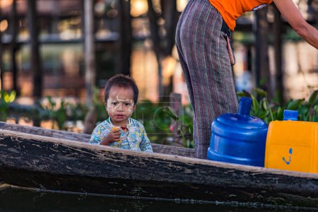 Téléchargez les photos : Un tout-petit avec de la crème solaire Thanaka birmane sur un bateau traditionnel en bois au lac Inle, Myanmar, Asie, le 12 avril 2018 - en image libre de droit