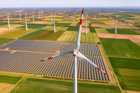 Foto de Vista aérea de cerca de una turbina eólica frente a campos agrícolas y paneles fotovoltaicos de un parque solar en crisis energética - Imagen libre de derechos
