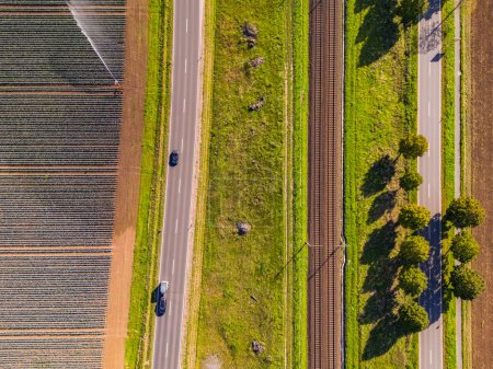 Photo for A railroad line with two tracks next to two roads and fields next to agricultural fields - Royalty Free Image