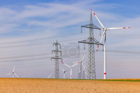 Foto de Campo con muchas turbinas eólicas de una turbina eólica y líneas eléctricas de varios polos de potencia bajo el cielo azul - Imagen libre de derechos