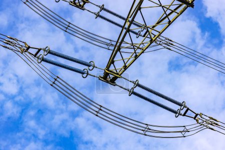 Téléchargez les photos : Lignes pour l'électricité avec isolateurs et câbles sur un pylône haute tension comme une vue vers le haut contre le ciel bleu - en image libre de droit