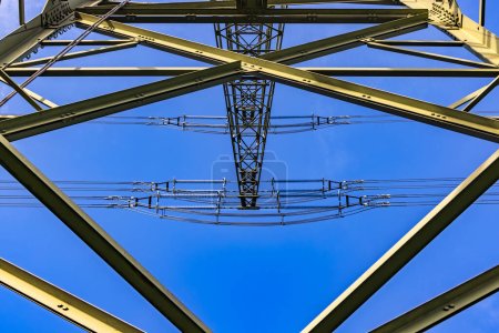 Foto de Mangueras y travesaños del esqueleto de acero de un poste de energía visto desde abajo contra el cielo azul - Imagen libre de derechos