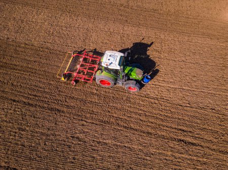 Photo for A green tractor with a red plow on a field with plowed soil seen from above as an aerial view - Royalty Free Image