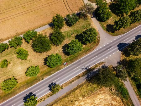 Photo for Country road with cycle path next to fields with trees and several dirt tracks in rural countryside - Royalty Free Image