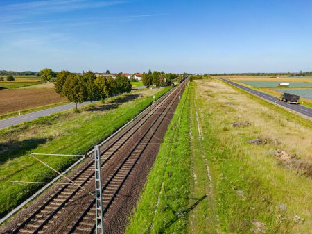 Photo for An electric railroad line with tracks next to two roads in a rural area, Germany - Royalty Free Image