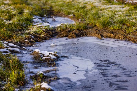 Field path with water, ice and ice crystals in a puddle in winter