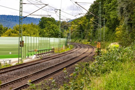 Dos vías paralelas de una línea ferroviaria discurren junto a una barrera acústica a través de la Baviera rural