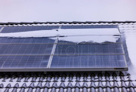 Solar modules covered with snow generate less electricity on a house roof in winter
