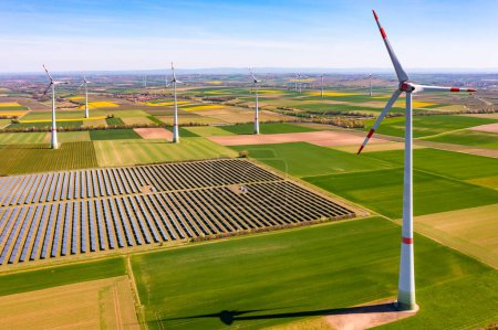 Generation of green energy in Germany by solar panels of a solar park and wind turbines up to the horizon as an aerial view