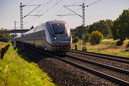 Ein ICE-Zug auf einem Gleis einer Bahnstrecke mit Feldern und Bäumen auf dem Land im Personenverkehr in Deutschland
