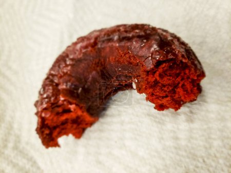 Blick auf einen teilweise verzehrten Donut aus rotem Samt, der auf einer Papierserviette sitzt