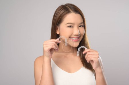 Una joven sonriente sosteniendo frenillos invisalign sobre el estudio de fondo blanco, la salud dental y el concepto de ortodoncia.