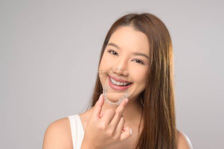 Foto de Una joven sonriente sosteniendo frenillos invisalign sobre el estudio de fondo blanco, la salud dental y el concepto de ortodoncia. - Imagen libre de derechos