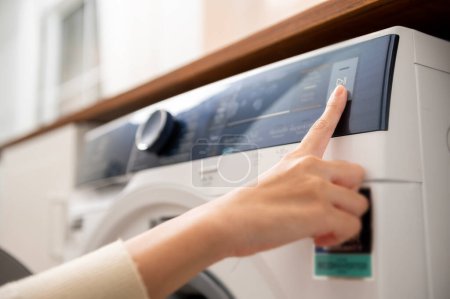 Téléchargez les photos : Gros plan femme main appuyant sur les boutons de la machine à laver pour programmer ou démarrer la lessive, concept de mode de vie des soins de santé - en image libre de droit