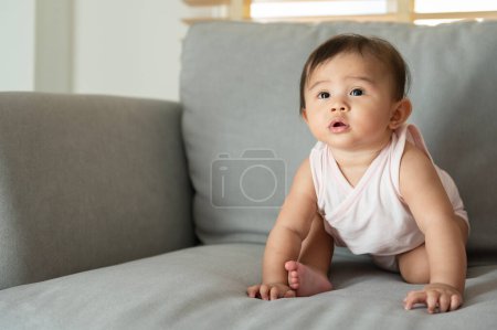 Téléchargez les photos : Portrait de bébé fille assise sur le canapé à la maison, famille, enfant, concept d'enfance et de parentalité - en image libre de droit