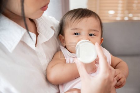 Téléchargez les photos : Une petite fille boit du biberon de lait dans les bras de la mère, la famille, l'enfant, l'enfance et la parentalité concept - en image libre de droit