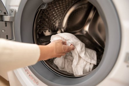 Téléchargez les photos : Fermer la main de la femme garde les vêtements dans la machine à laver, concept de mode de vie des soins de santé - en image libre de droit